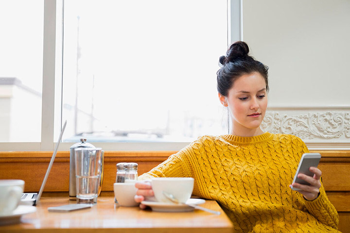 Woman texting and drinking cappuccino in cafe